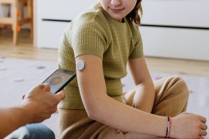 Diabetic girl with a CGM sensor on her arm. Father using an app to monitor blood sugar levels.