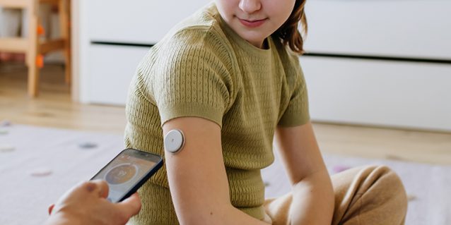 Diabetic girl with a CGM sensor on her arm. Father using an app to monitor blood sugar levels.
